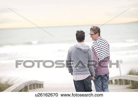 Stock Image - Gay couple chatting on beach. Fotosearch