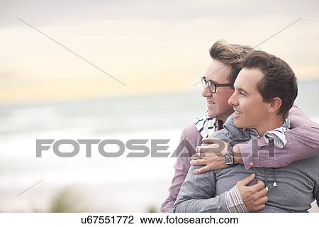 Stock Image - Gay couple hugging on beach. Fotosearch