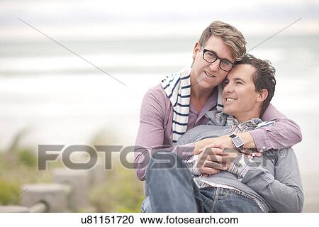 Stock Image - Gay couple hugging on beach. Fotosearch