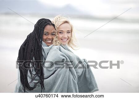 Picture - Gay couple wrapped in blanket on beach. Fotosearch