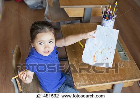 Stock Image - Girl at desk showing picture, high angle. Fotosearch