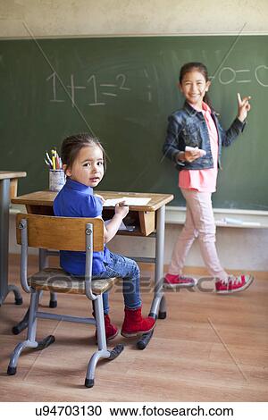 Girl by blackboard and sister at desk View Large Photo Image Stock Image - Girl by blackboard and sister at desk. Fotosearch