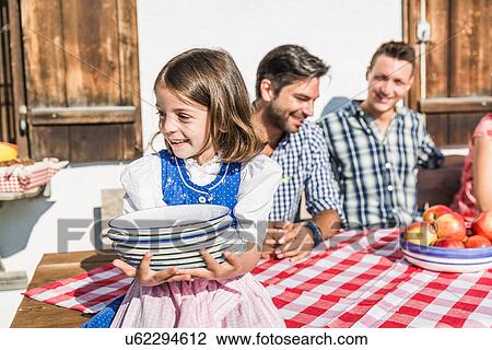 Stock Image - Girl carrying breakfast plates outside chalet, Tyrol, Austria. Fotosearch