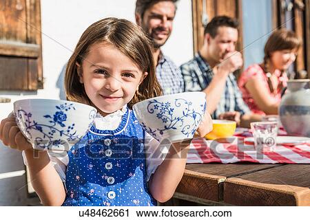 Stock Image - Girl holding breakfast cups outside chalet, Tyrol, Austria. Fotosearch