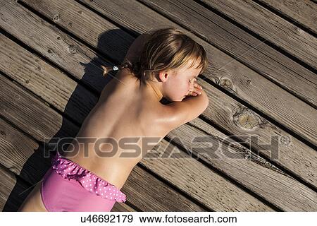 Stock Photo - Girl lying on front on pier with eyes closed. Fotosearch