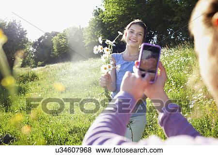 Stock Photo - Girl taking photograph of girl picking flowers. Fotosearch