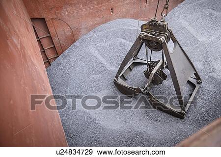 Stock Photo - Grab unloading metal alloy from ship's hull. Fotosearch