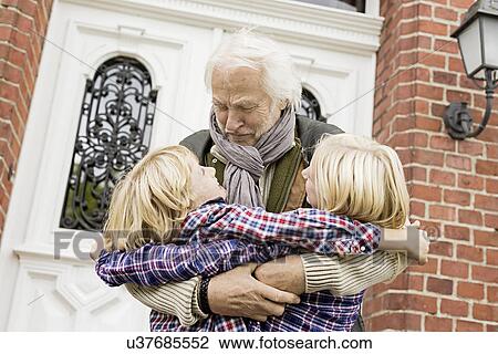 Stock Image - Grandfather hugging grandchildren by front door. Fotosearch