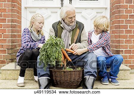 Picture - Grandfather sitting with grandchildren on doorstep with carrots. Fotosearch