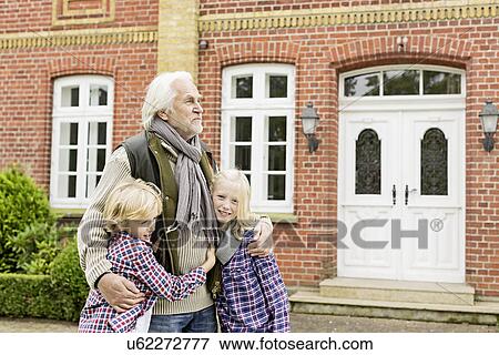 Grandfather with arms around grandchildren outside house View Large Photo Image Stock Photo - Grandfather with arms around grandchildren outside house. Fotosearch