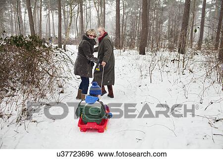 Stock Photograph - Grandparents pulling grandson on toboggan in snow. Fotosearch