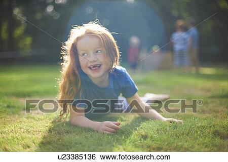 Happy young girl lying on grass in garden View Large Photo Image Stock Photograph - Happy young girl lying on grass in garden. Fotosearch