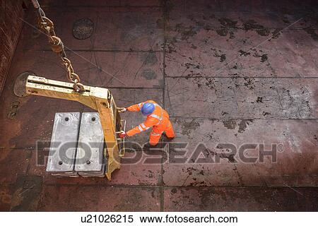 Stock Photography - High angle view of worker unloading metal alloy ingots from ship's hold. Fotosearch