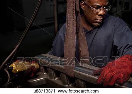 Stock Image - Lifting up a rack bar to be machined. Fotosearch