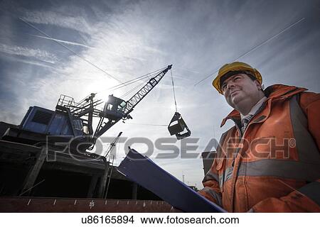 Picture - Low angle view of load master checking ship loading. Fotosearch