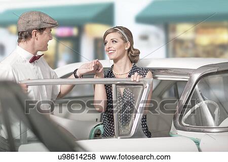 Stock Photo - Man helping woman out of vintage car. Fotosearch