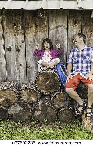 Stock Photograph - Man smiling at little girl in yoga pose on cut logs. Fotosearch