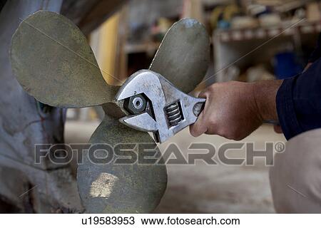 Stock Image - Man tightening boat propeller in workshop. Fotosearch