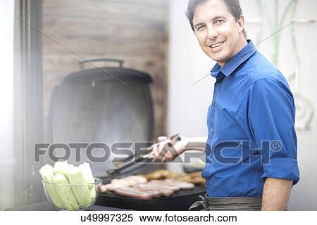 Stock Photography - Mature man barbecuing sausages. Fotosearch