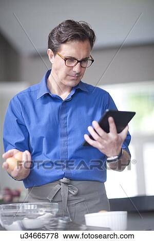 Mature man holding eggs, looking at digital tablet View Large Photo Image Stock Photo - Mature man holding eggs, looking at digital tablet. Fotosearch
