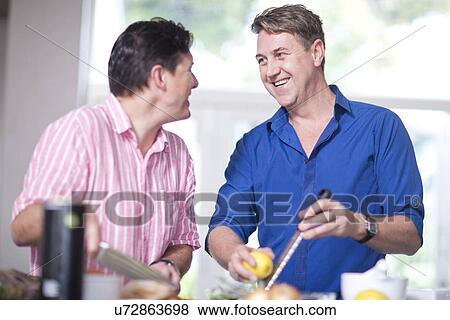 Stock Photo - Mature men in kitchen, one grating lemon zest. Fotosearch