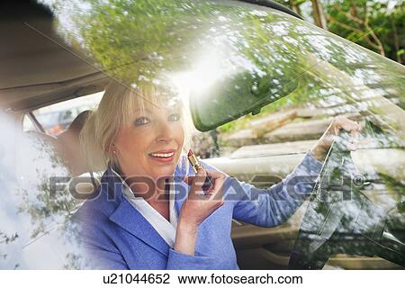 Mature woman applying lipstick in car View Large Photo Image Stock Image - Mature woman applying lipstick in car. Fotosearch
