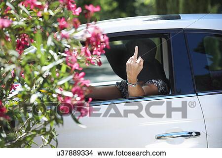 Picture - Mature woman driving car, sticking finger up. Fotosearch