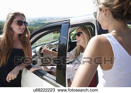 Stock Image - Mature woman sitting in car, talking to teenagers. Fotosearch