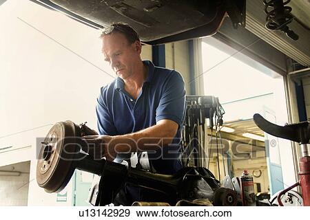 Stock Photo - Mechanic repairing car in workshop. Fotosearch