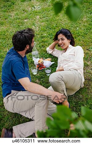 Stock Image - Mid adult couple having picnic on lawn. Fotosearch