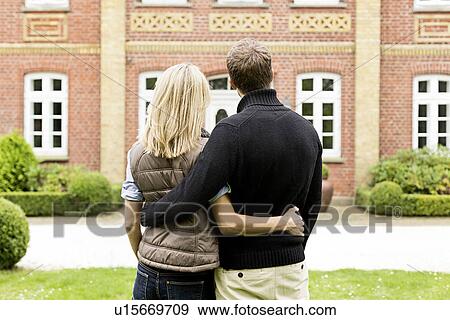 Stock Photo - Mid adult couple looking at house, rear view. Fotosearch
