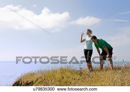 Stock Image - Mid adult couple resting from exercise, Thurlestone, Devon, UK. Fotosearch