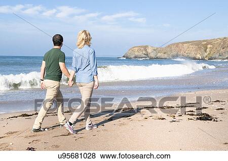 Stock Photo - Mid adult couple walking on beach, Thurlestone, Devon, UK. Fotosearch