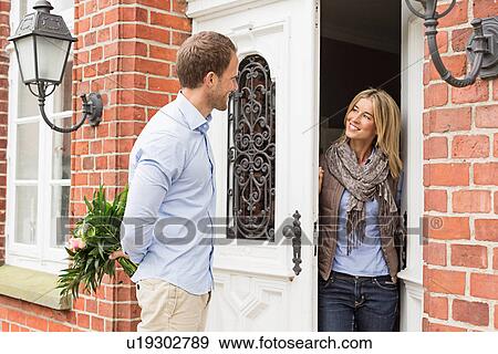 Stock Photo - Mid adult couple, woman opening front door. Fotosearch