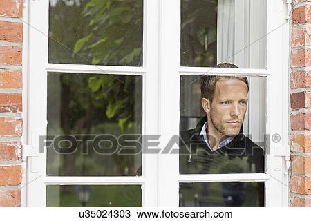 Stock Image - Mid adult man looking out of window. Fotosearch