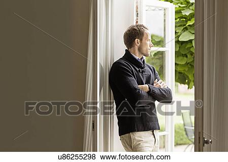 Stock Photo - Mid adult man looking out of window, arms folded. Fotosearch
