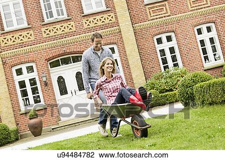 Mid adult man pushing woman in wheelbarrow View Large Photo Image Stock Image - Mid adult man pushing woman in wheelbarrow. Fotosearch