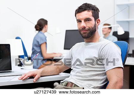 Mid adult man sitting at desk in office View Large Photo Image Stock Photo - Mid adult man sitting at desk in office. Fotosearch