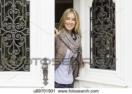 Stock Image - Mid adult woman opening front door. Fotosearch