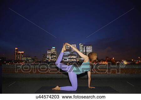 Mid adult woman practicing yoga on city rooftop at night View Large Photo Image Stock Image - Mid adult woman practicing yoga on city rooftop at night. Fotosearch