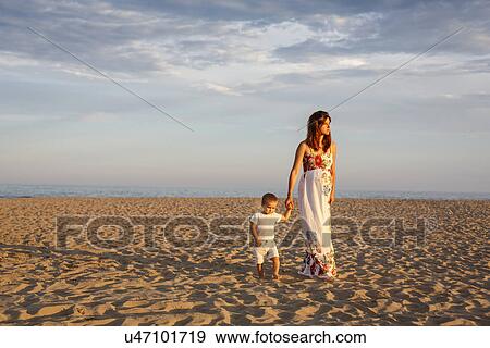 Stock Photo - Mother and toddler walking along beach, holding hands. Fotosearch