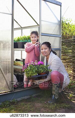 Stock Image - Mother holding plants with daughter in greenhouse. Fotosearch