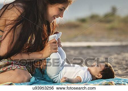 Mother looking down at baby lying on rug View Large Photo Image Stock Photograph - Mother looking down at baby lying on rug. Fotosearch