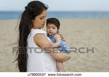 Stock Photo - Mother on beach carrying baby in arms. Fotosearch