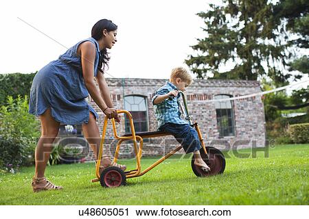 Stock Image - Mother pushing son on tricycle. Fotosearch