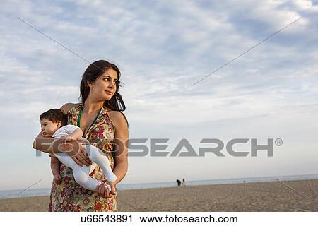 Mother standing on beach holding baby View Large Photo Image Stock Image - Mother standing on beach holding baby. Fotosearch