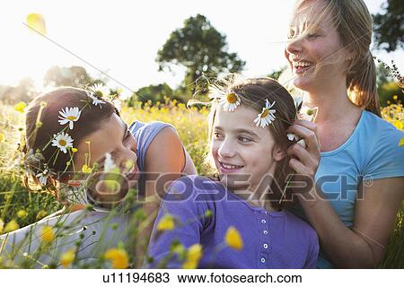 Stock Image - Mother tying daisy chain around daughter's head. Fotosearch