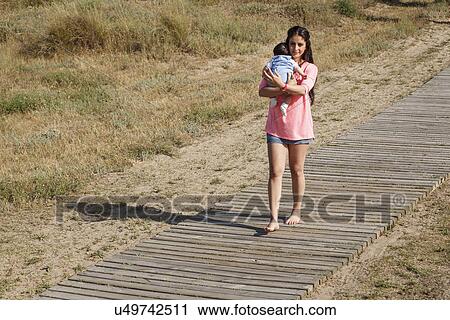 Mother walking along boardwalk carrying baby in arms View Large Photo Image Stock Image - Mother walking along boardwalk carrying baby in arms. Fotosearch
