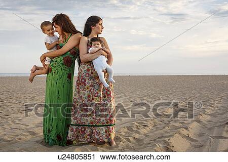 Stock Image - Mothers standing on beach holding baby and toddler. Fotosearch