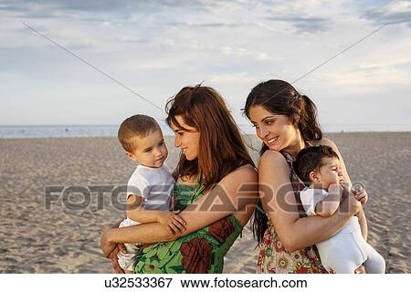 Mothers standing on beach holding baby and toddler View Large Photo Image Stock Photo - Mothers standing on beach holding baby and toddler. Fotosearch